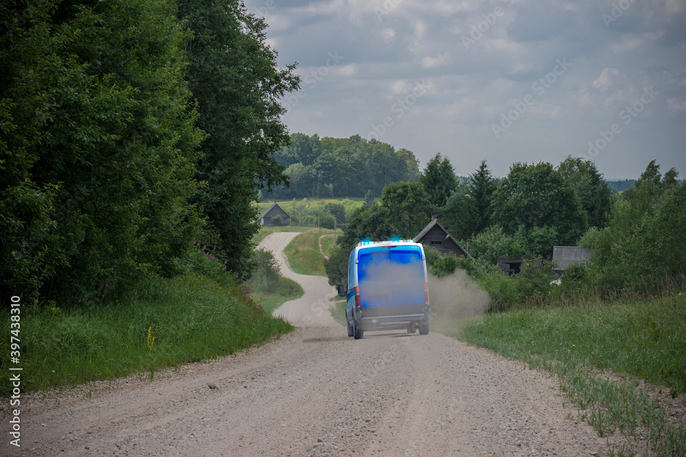 A police van with blue flasher lights blinking rushing to a crime scene on a gravel road in the countryside