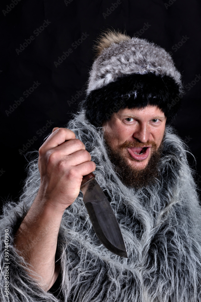 Bearded hunter dressed in a fur mantle and fur hat with knife Bearded hunter dressed in a fur mantle and fur hat with knife