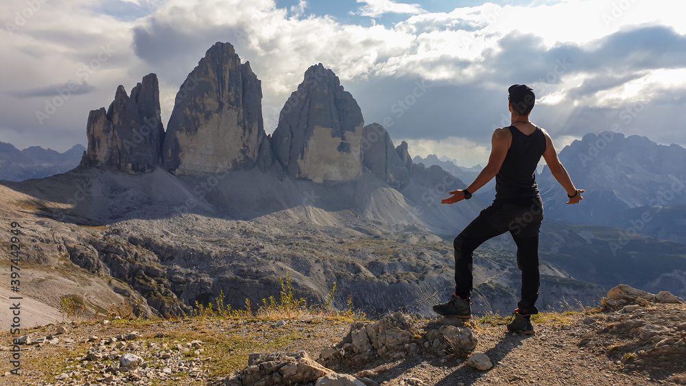 A man in hiking outfit standing with his arms wide open and enjoying the view on the famous Tre Cime di Lavaredo (Drei Zinnen), mountains in Italian Dolomites. Desolated and raw landscape. Freedom