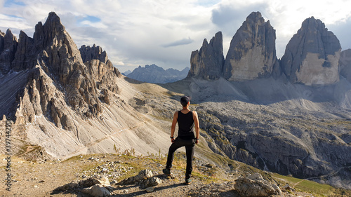 A man in hiking outfit standing on top of Sextner Stein and enjoying the view on the famous Tre Cime di Lavaredo (Drei Zinnen), mountains in Italian Dolomites. Desolated and raw landscape. Freedom