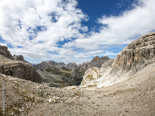 A panoramic view on Dolomites in Italy. There are sharp and steep mountain slopes around. Lots  of lose stones and pebbles. The sky is full of soft clouds. Raw landscape. Serenity and calmness © Chris