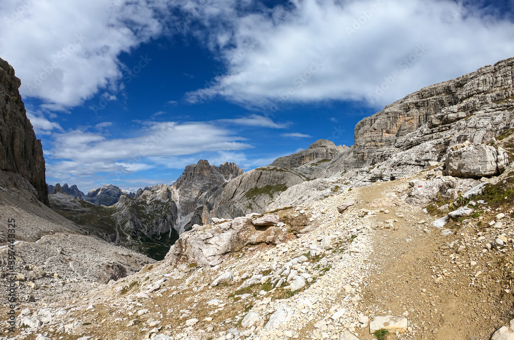 A panoramic view on Dolomites in Italy. There are sharp and steep mountain slopes around. Lots of lose stones and pebbles. The sky is full of soft clouds. Raw landscape. Serenity and calmness A panoramic view on Dolomites in Italy. There are sharp and steep mountain slopes around. Lots of lose stones and pebbles. The sky is full of soft clouds. Raw landscape. Serenity and calmness