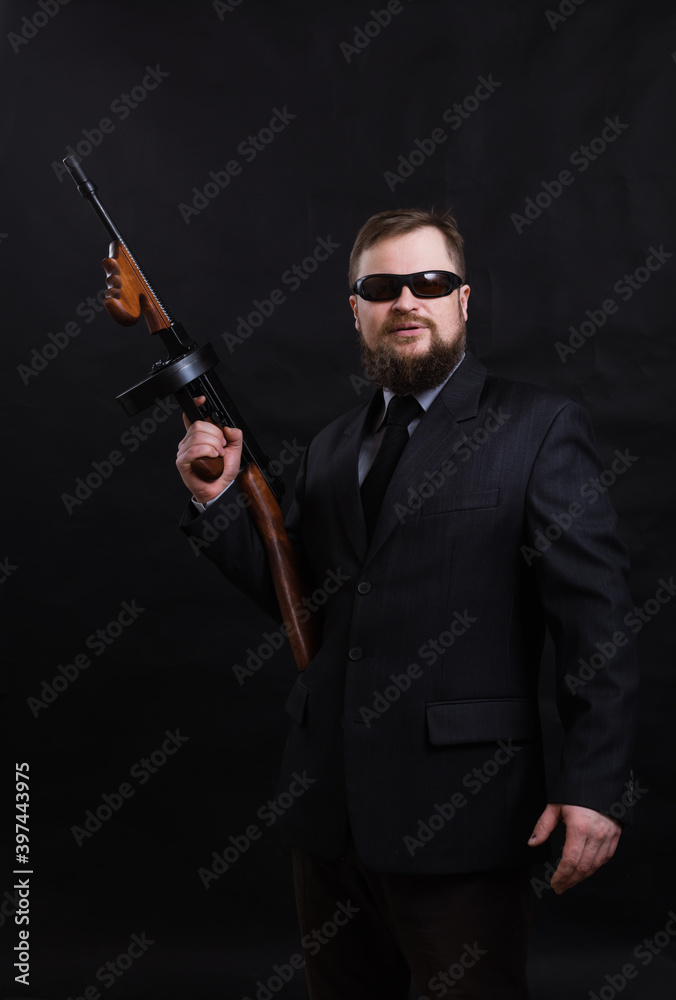 Mature bearded man in sunglasses dressed in suit with tommy gun Mature bearded man in sunglasses dressed in suit with tommy gun