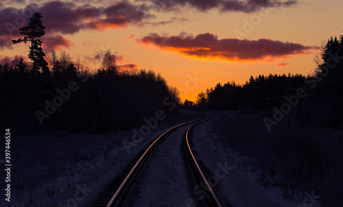 A beautiful winter morning landscape of a railway tracks in the forest. Colorful sunrise scenery of Northern Europe.
