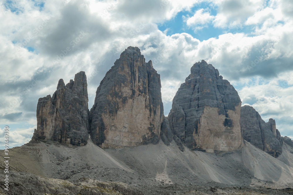 A capture of the famous Tre Cime di Lavaredo (Drei Zinnen) in Italian Dolomites. The mountains are surrounded by thick clouds. There is a lot of landslides and lose stones around. Natural wonder.