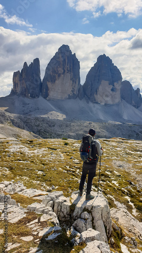 A man in hiking outfit enjoying the view on the famous Tre Cime di Lavaredo (Drei Zinnen), mountains in Italian Dolomites. Desolated and raw landscape, full of lose stones. Overcast. Achievement