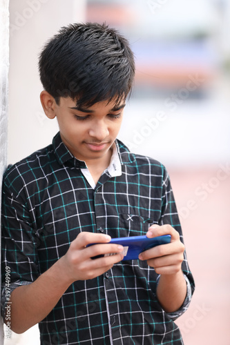 Portrait of Indian young boy playing game using mobile phone at home terrace 