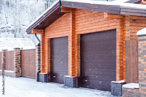 Large plan light brick garage for two cars with automatic gates in a winter village, soft focus and snowfall. Winter country life