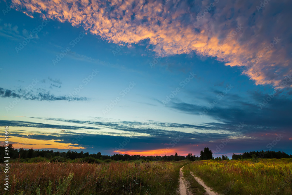Road to the field and sky with clouds on sunset. Summer landscape.
