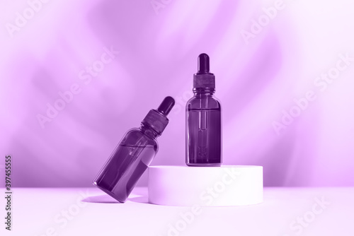 Glass dropper bottles with a pippette with black rubber tip on the beautiful purple shadow background. Nature Skin concept. Organic Spa Cosmetics. Trendy color of the year.
