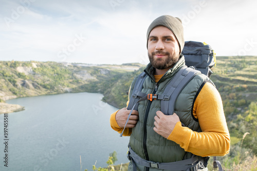 Happy young male backpacker standing against river surrounded by mountains