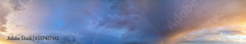 Summer sunset after rain sky panorama with fleece purple clouds and rainbow. Evening dusk good weather natural cloudscape background.