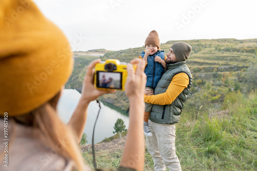 Young female with photocamera taking photograph of her husband and little son