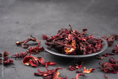 Hibiscus tea dried flowers in round plate on gray concrete background. Vitamin, recipe, beverage concept. Close-up, copy space