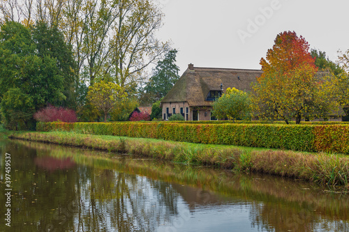 Traditional Dutch farmhouse with thatched rood reflected in a canal during autumn in Drente, Netherlands