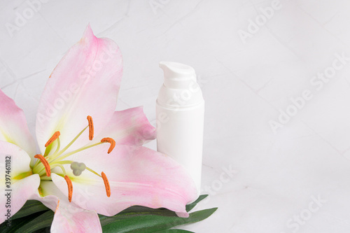 Bottle of face and body cream on white marble background, spa salon concept, lily flower, tropical. Copy space