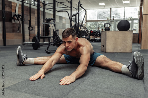 Young muscular man practicing muscle stretching in modern health club