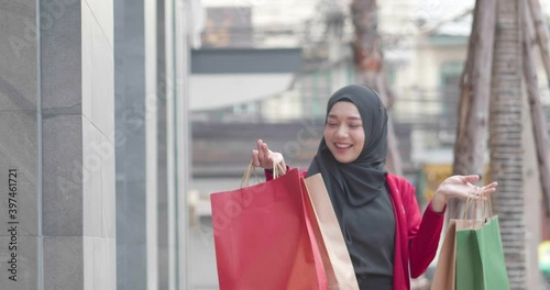 Muslim woman happy walking with carry many shopping bag and enjoy rotation dancing in outdoor city. Smiling female hobby on holiday with discount sales product wear black hijab and red clothes