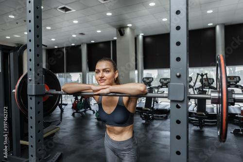 Young athletic woman resting leaning on barbell in gym