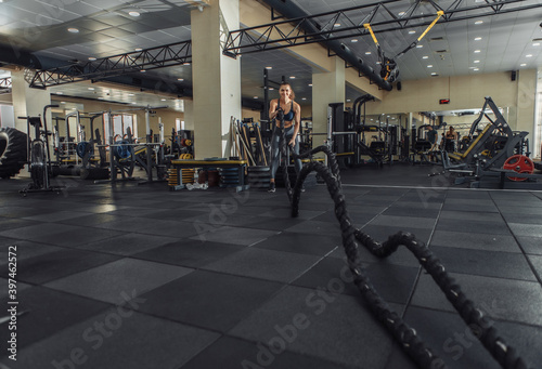 Athletic woman trains with battle ropes in the modern gym. Cross training