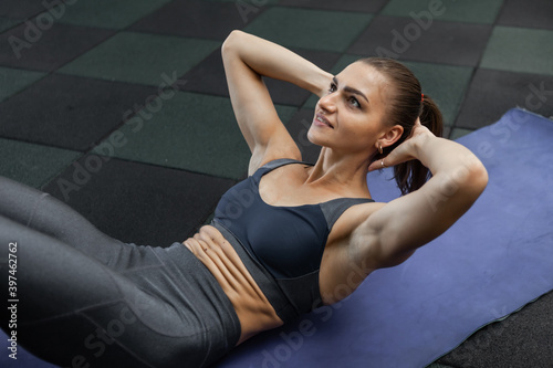 Crunches for the abdominal muscles. Young fit woman trains abdominal muscles lying on the mat in the gym