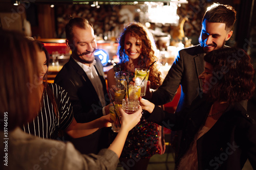 Group of friends cheering and drinking cocktails together at the bar. Young people celebrating winter holiday together with coctails at a nightclub party. Youth  lifestyle  drink  birthday concept. 