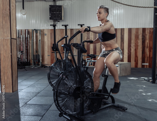 Muscular Woman exercising on air bike. Cycling fitness training. Athletic female using air bike cardio workout. Cross functional training.