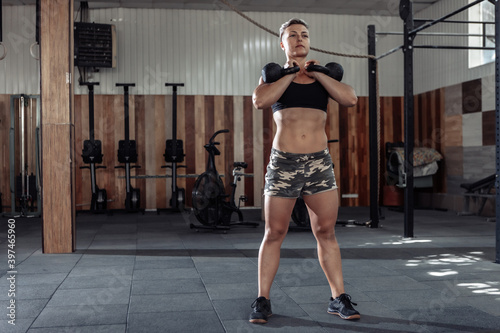 Muscular woman athlete holding heavy kettlebells. Functional, cross training in a modern gym.
