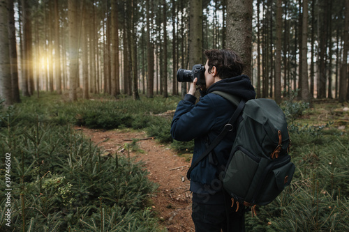 The tourist takes a picture with his camera on his trip in a beautiful forest at sunset. A small hiking trail conifers and fir trees.