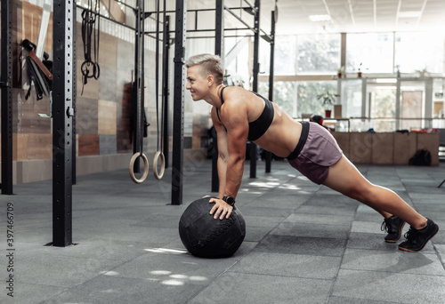 Muscular athletic woman push ups with medicine balls in a modern gym. Cross fit, functional training