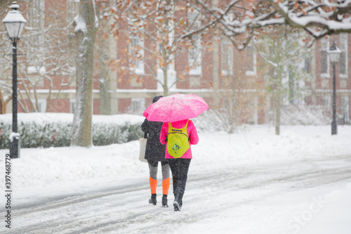 Students walking in a snowstorm and holding an umbrella on a college campus