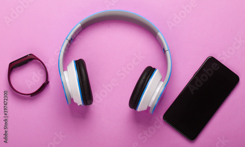 Flat lay composition of modern gadgets. Wireless headphones, smart bracelet, smartphone on pink background. Millennial stuff. Top view