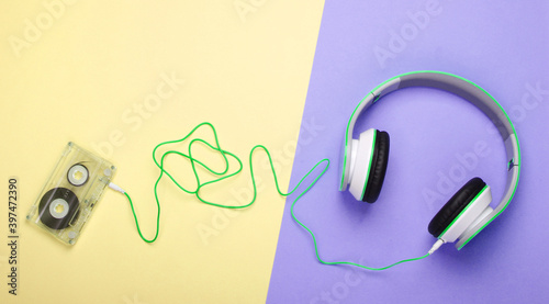 Stylish wired stereo headphones with audio cassette on colored pastel background. Music lover. Retro 80s. Top view.