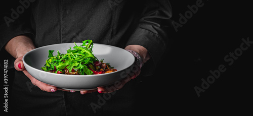 chef in a black suit holds in his hands bowl with salad on Dark grey black background