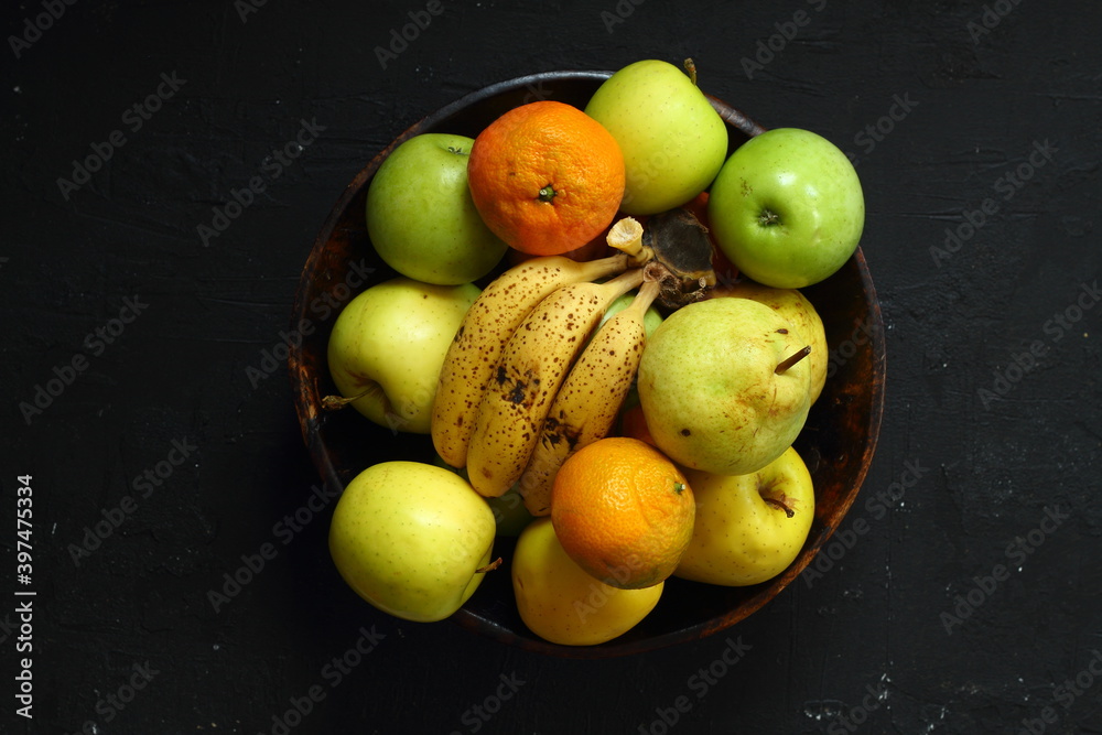 a lot of ripe and juicy fruit on a black background. Apples, pears, banana  and Mandarin together.