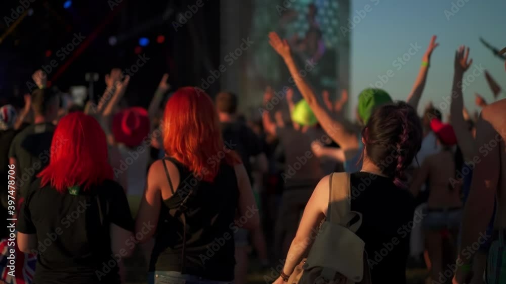 Crowd of people enjoying the concert. Hipster woman singing and dancing. Sunset light and smoke at rock festival. Teens applauding and waving hands. Concept of music and lifestyle.