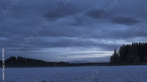 Zeitraffer Abenddämmerung im Alpenvorland im Winter mit schneebedecktem See und ziehenden Wolken 