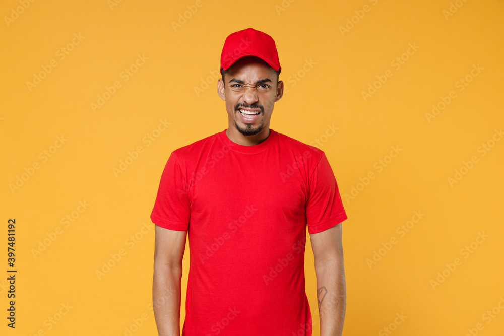 Delivery employee african man 20s in red cap blank print t-shirt uniform workwear work courier dealer service during quarantine coronavirus covid-19 virus concept isolated on yellow background studio. Delivery employee african man 20s in red cap blank print t-shirt uniform workwear work courier dealer service during quarantine coronavirus covid-19 virus concept isolated on yellow background studio.