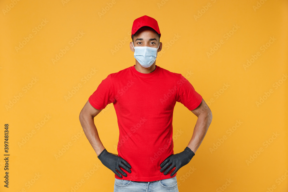 Delivery employee african man in red cap blank print t-shirt face mask gloves uniform work courier dealer service on quarantine coronavirus covid-19 virus concept isolated on yellow background studio. Delivery employee african man in red cap blank print t-shirt face mask gloves uniform work courier dealer service on quarantine coronavirus covid-19 virus concept isolated on yellow background studio.