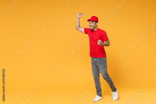 Full length delivery employee african man 20s in red cap blank print t-shirt uniform workwear work courier dealer service during quarantine covid-19 virus concept isolated on yellow background studio. © ViDi Studio