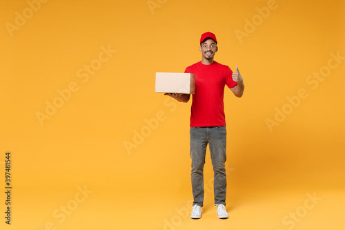 Full length delivery employee african man 20s in red cap blank print t-shirt uniform work courier service on quarantine covid-19 virus concept hold cardboard box isolated on yellow background studio.