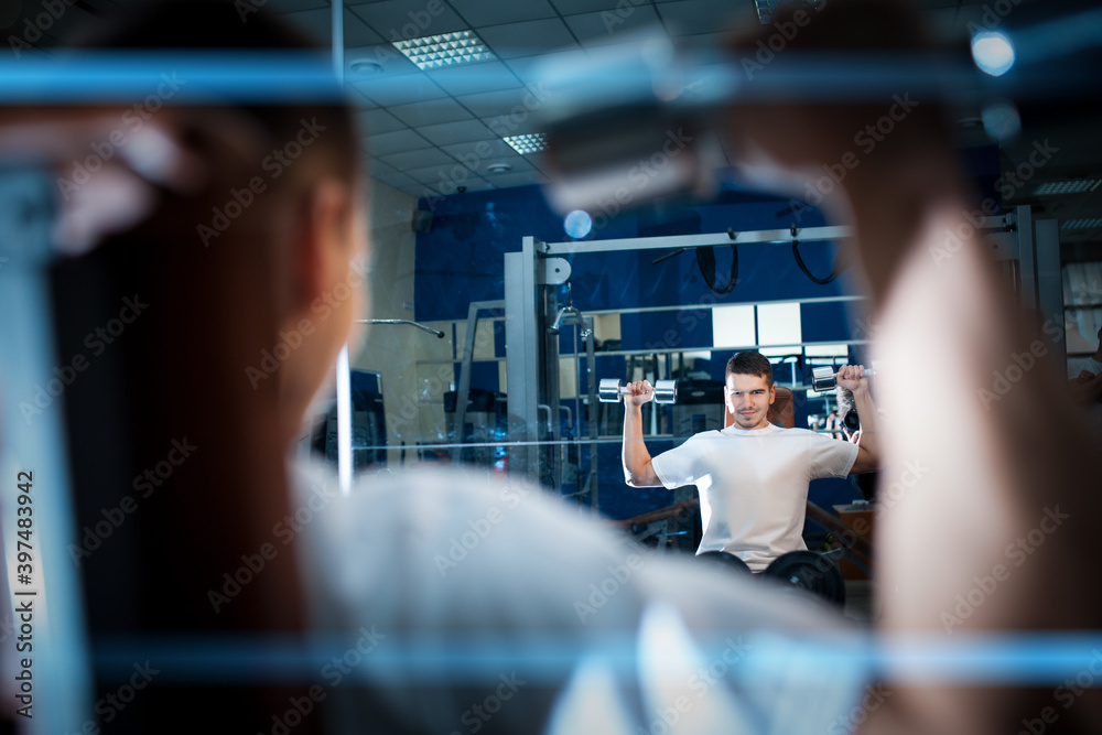 young handsome male has personal workout or exercising with dumbbells in gym