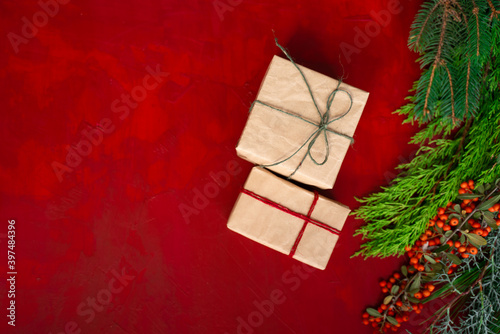 gift boxes covered with craft paper, with tree branches and hawthorn for christmas on red wooden background top view photo