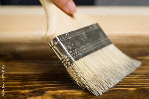 A close-up paint brush that paints a wooden table with brown stain or paint, with the appearance of wood texture. Woodwork, painting boards.