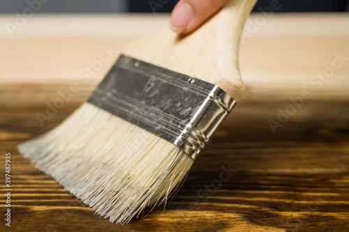 A close-up paint brush that paints a wooden table with brown stain or paint, with the appearance of wood texture. Woodwork, painting boards.