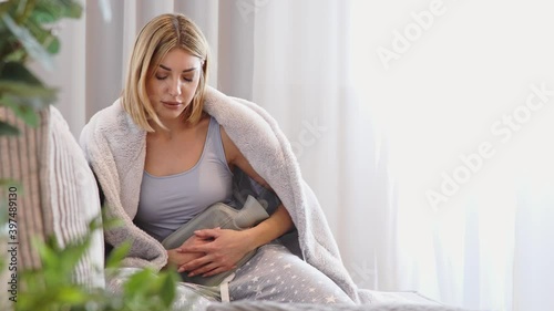 Stomach ache. A young woman warms her aching belly with a hot water bottle. Menstrual pain, colic and stomach discomfort.  photo