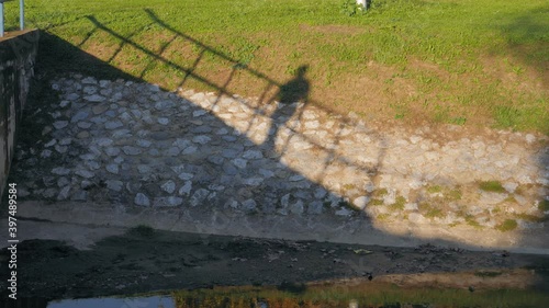The shadow of a man walking along a fence above a stream. Slow motion shot.
