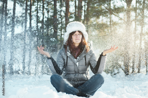 Young woman with closed eyes meditates in winter forest during snowfall. Tranquility and concentration concept.