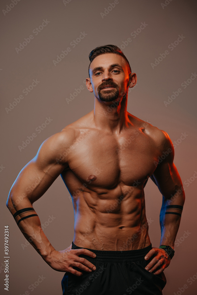 A muscular man with a beard is posing. The athletic guy is demonstrating his sporty physique. An athlete is relaxing after hard training.