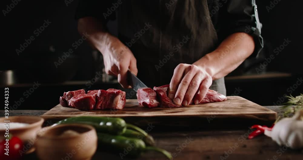 Chef cutting meat with a knife on kitchen table. Cooker is making a meal out of beef and vegetables on professional kitchen 4k footage